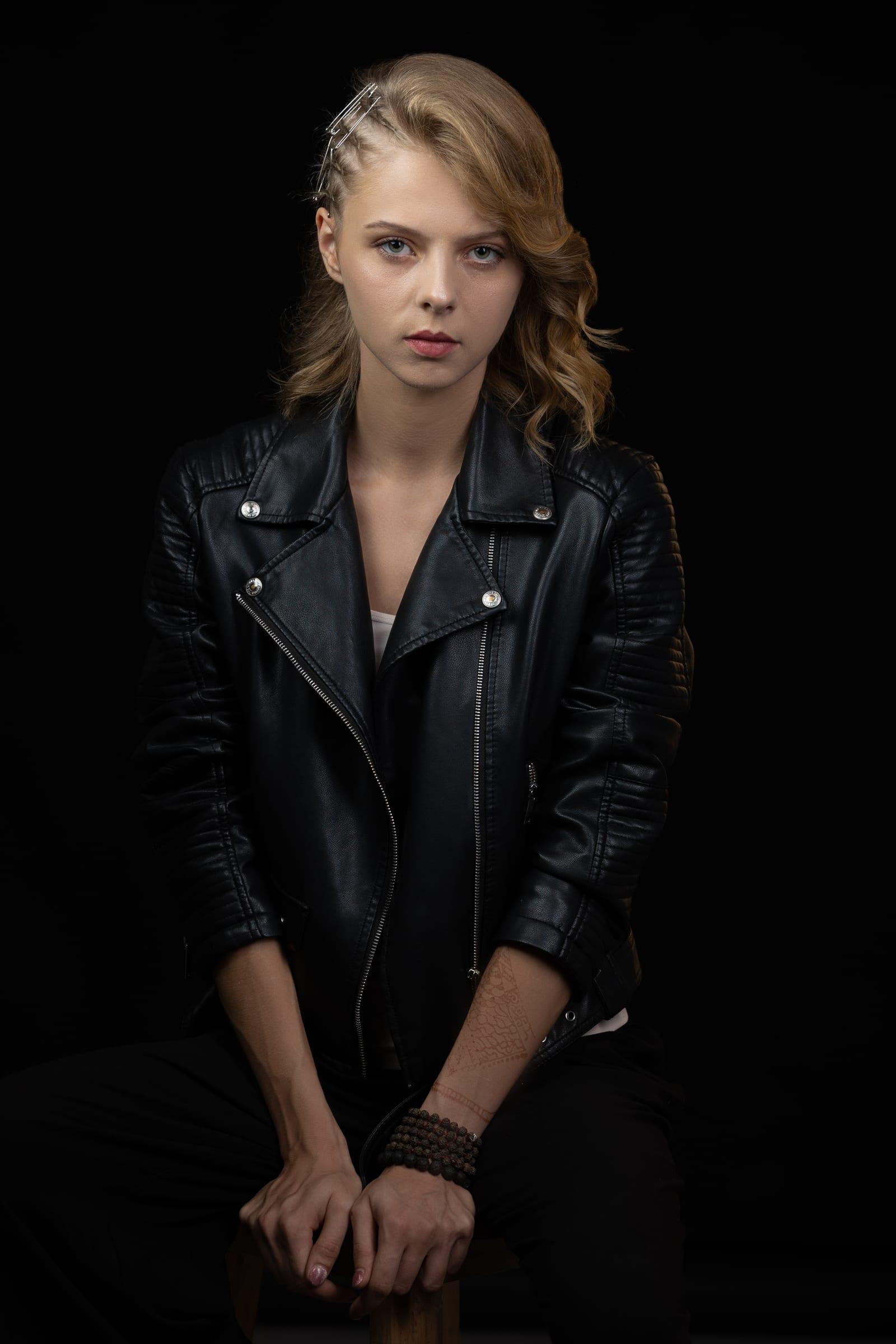 Seated studio portrait of a woman in a black leather jacket against a dark backdrop